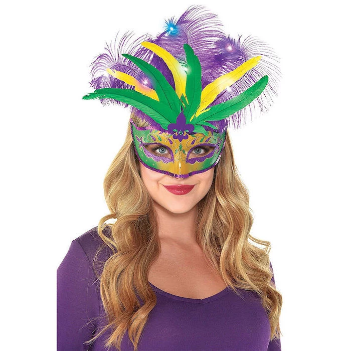 blonde woman, wearing purple blouse, masquerade party masks, gold mask with green and purple decorations and feathers