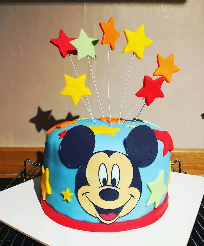 one tier cake, covered with blue fondant, colorful fondant stars cake toppers, mickey mouse cakes 1st birthday