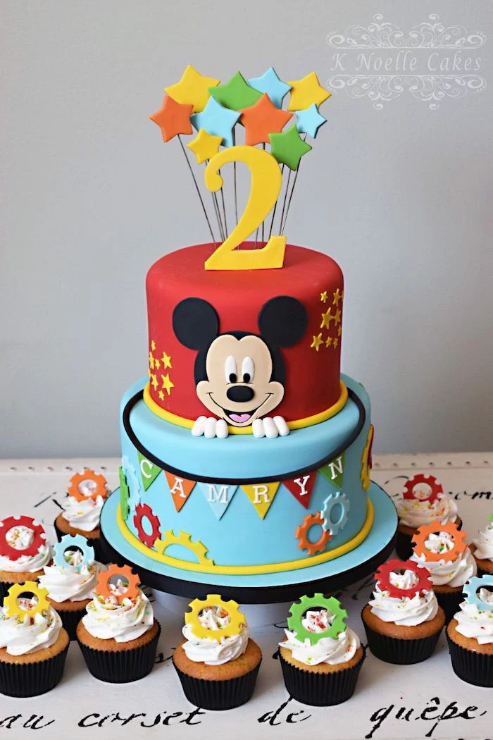 two tier cake, covered with red and blue fondant, mickey mouse cakes 1st birthday, cupcakes arranged around it