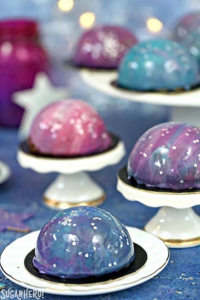 mini galaxy cakes, placed on white cake stands, decorated with white stars sprinkles, how to make glaze for cake