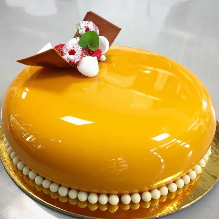 one tier cake covered with orange glaze, mirror glaze cake recipe, raspberry decorations on top, placed on gold tray