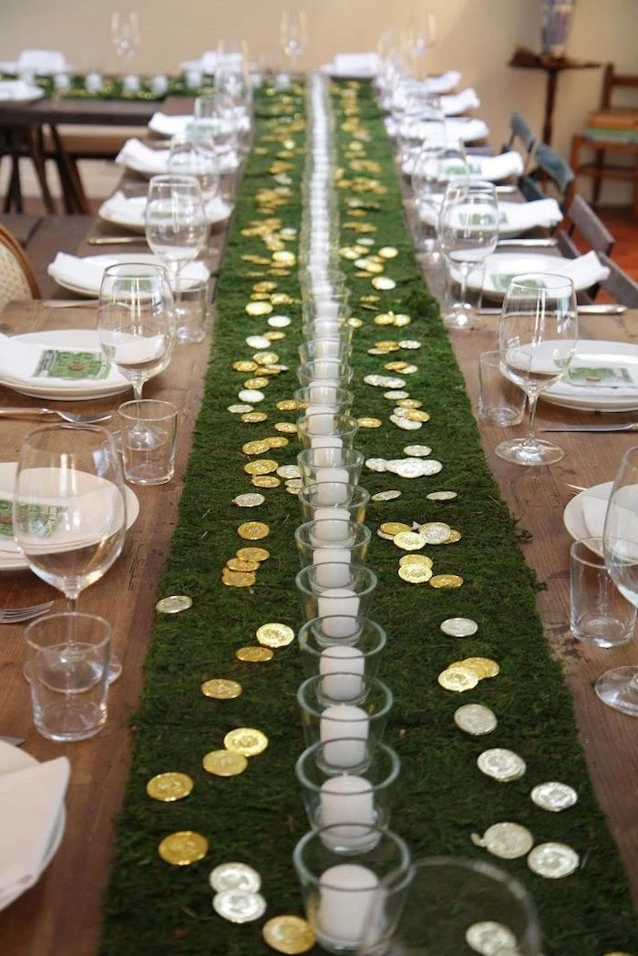 moss table runner, st patricks decor, gold coins scattered on it, around glasses with candles inside, table settings on both sides