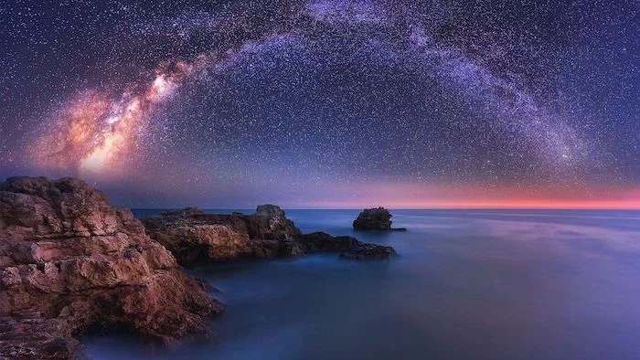 ocean landscape, rocks on the beach next to the water, space wallpaper 4k, galaxy sky filled with stars above the water