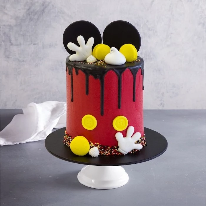 one tier cake, covered with red fondant, chocolate dripping on the sides, mickey mouse smash cake, placed on black cake stand