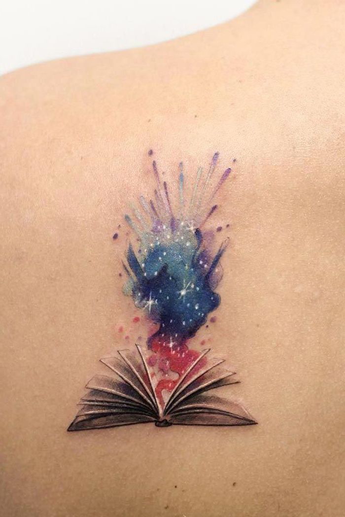 open book with a galaxy coming out of it, purple blue and pink galaxy with stars, small space tattoos, back of shoulder tattoo