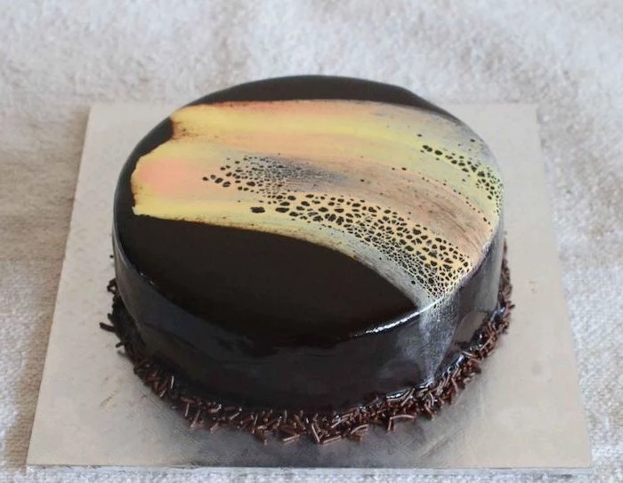 one tier cake with black and yellow glaze, mirror glaze cake recipe, chocolate sprinkles around it, placed on silver tray