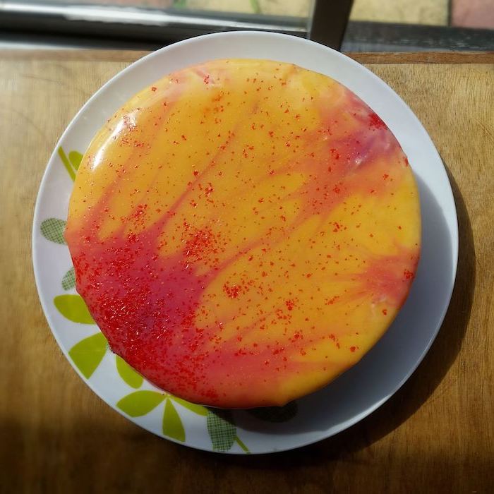 orange and yellow glaze on one tier cake, mirror glaze cake recipe, placed on white and green plate on wooden surface