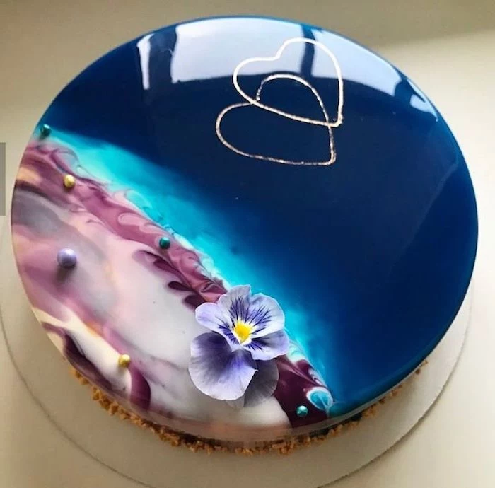 blue and purple glaze on tier cake, glaze icing for cake, flower and hearts decorations on top, placed on white tray
