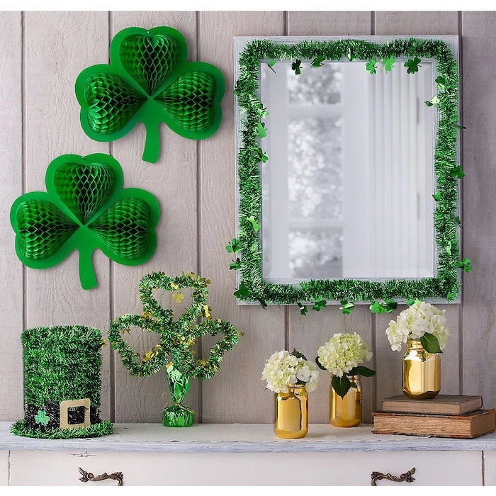 mirror hanging over a cupboard, decorated with green garlands, green paper shamrocks on the wall, st patrick's day decorations