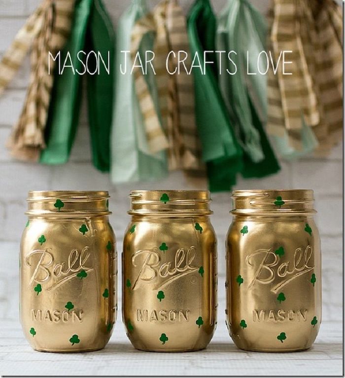 mason jars painted in gold, small green shamrocks painted on them ,st patricks day crafts, placed on white surface