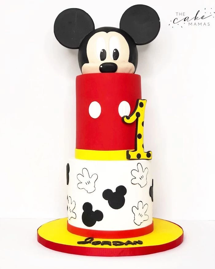 three tier cake, covered with black and white, red and yellow fondant, mickey mouse cake pan, placed on yellow cake tray