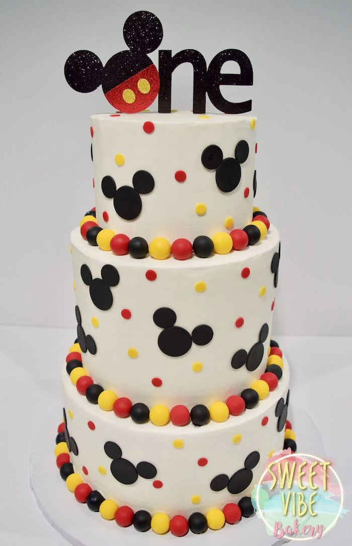 mickey mouse cake pan, three tier cake, covered with white fondant, black red and yellow decorations on it