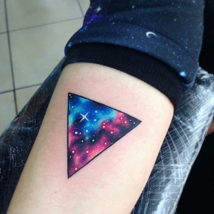 forearm geometrical triangle tattoo, milky way tattoo, pink blue and purple galaxy with stars inside the triangle