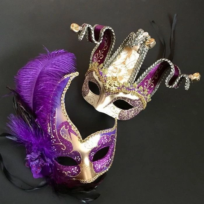 two gold masks, decorated with purple glitter, mens mardi gras masks, bells at the end, purple feathers