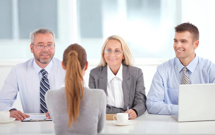 on woman and two men, dressed in business attire, sitting across from a blonde woman, job interview