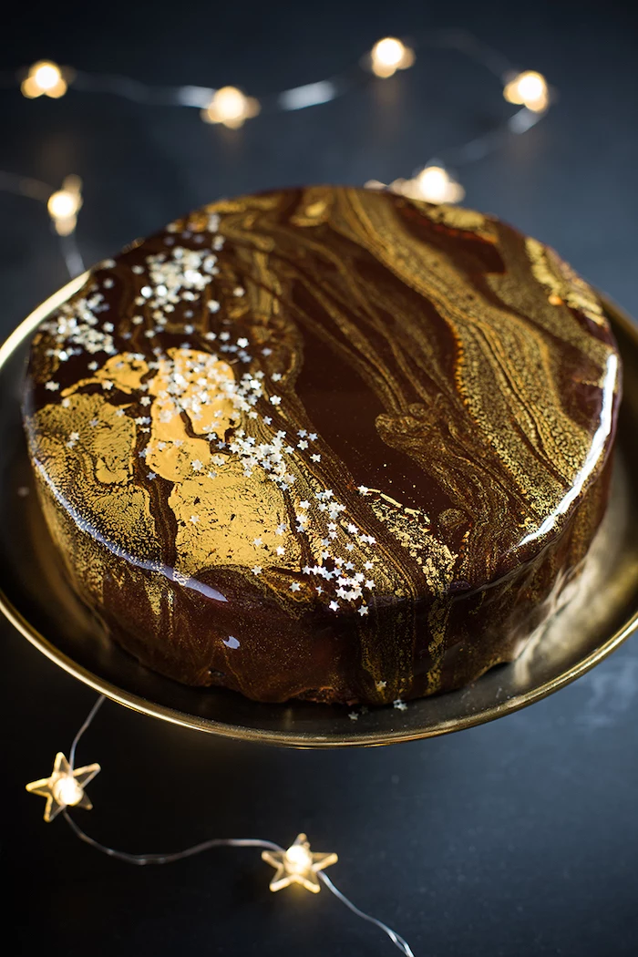 how to make mirror glaze, one tier cake with brown gold marble glaze, white stars sprinkles on top, fairy lights around