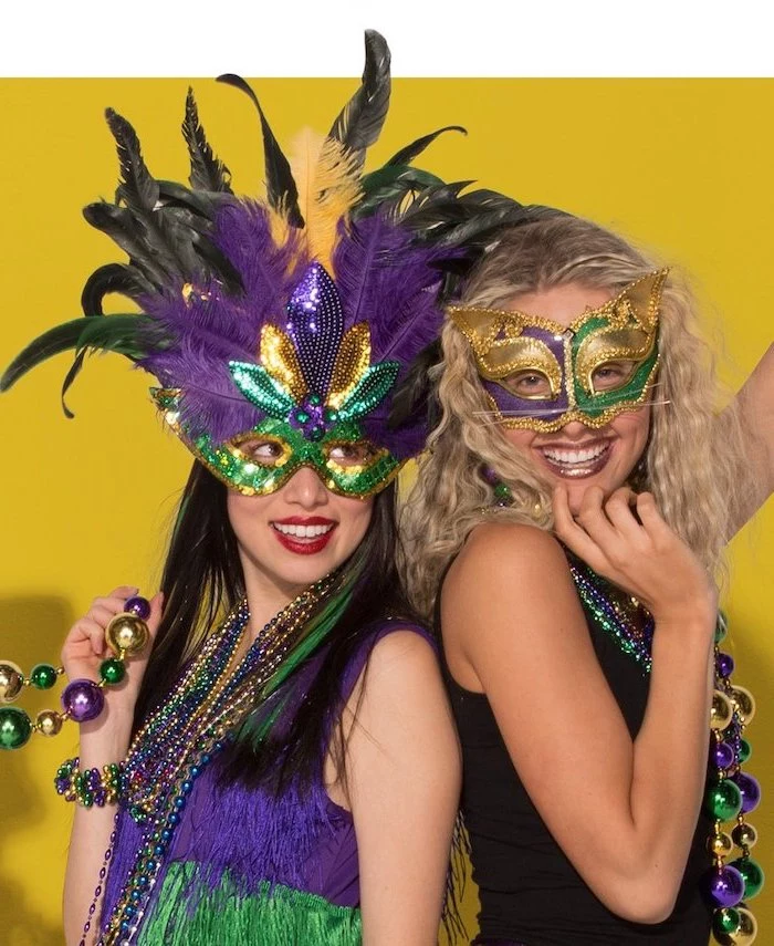 two women smiling, posing for a photograph, wearing different masks, decorated in purple gold and green, mens mardi gras masks
