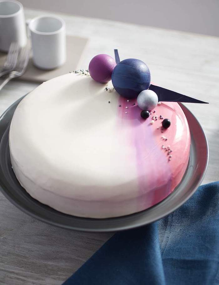 white pink and orange glaze on one tier cake, how to make mirror glaze, planets decorations on top, placed on grey plate