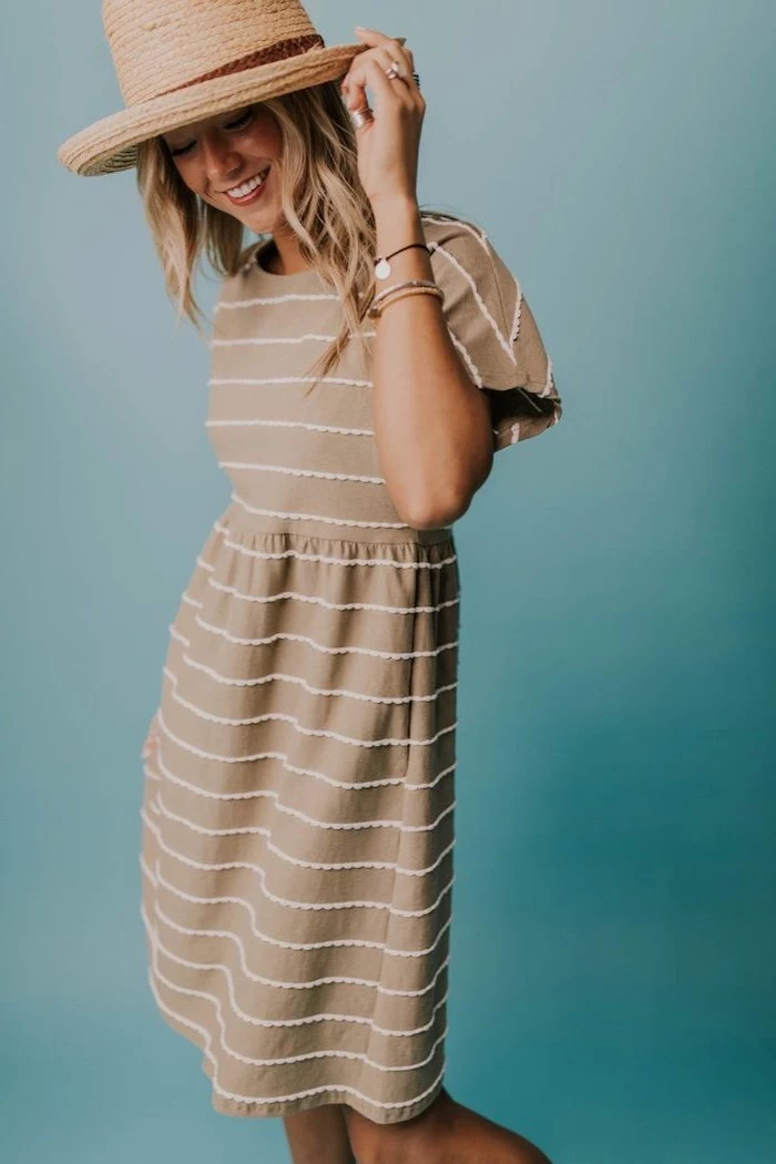 blonde woman wearing a hat on her head, easter dresses for women, wearing a beige dress with white stripes, blue background