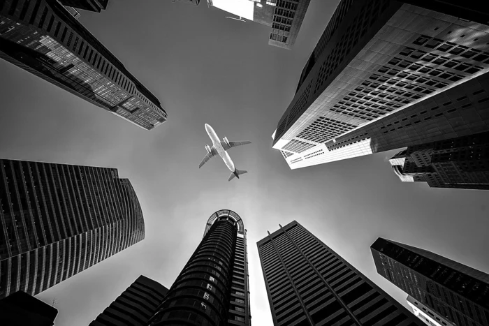 cheapest flights, black and white photo, airplane flying low above tall skyscrapers