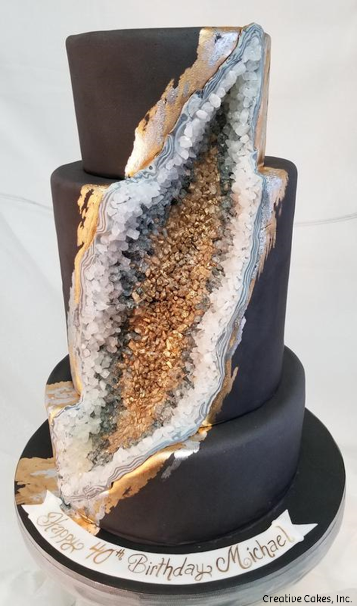 three tier cake, covered with black fondant, what is a geode cake, decorated with gold and grey rock candy