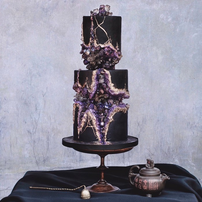 two tier cake, covered with black fondant, geode cake, placed on black cake stand, decorated with purple rock candy