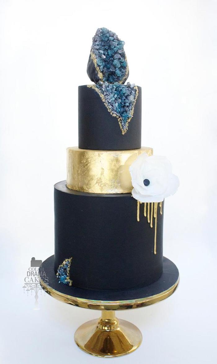 three tier cake, covered with navy blue and gold fondant, placed on gold cake stand, rock candy painted in blue, geode cake