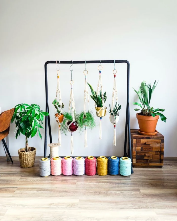 black metal clothing rack, pots with plants hanging from it, how to make a macrame plant hanger, colorful yarn on wooden floor