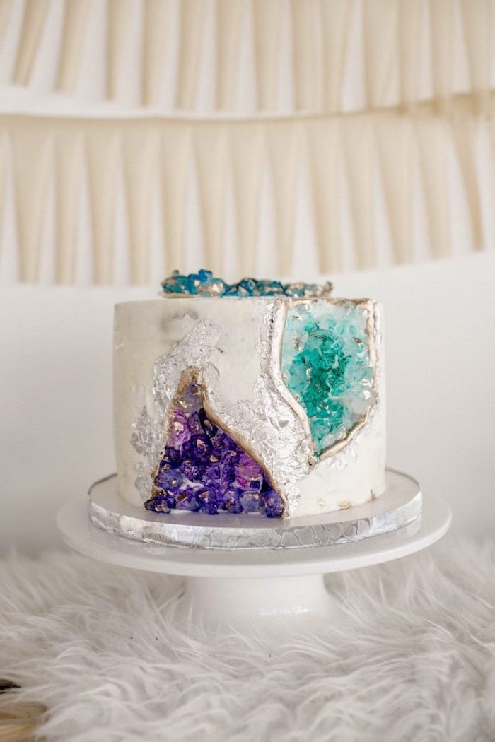 one tier cake, covered with white fondant, crystal cake, decorated with turquoise and purple rock candy, placed on white cake stand