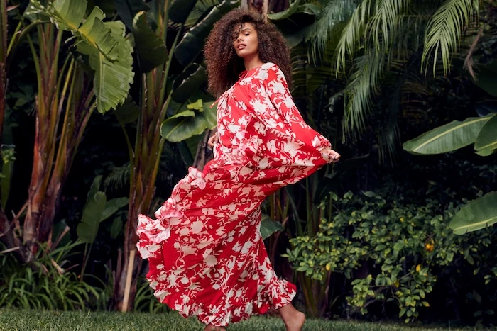 sunflower dress, woman with brown curly hair, wearing a long red dress with floral print, palm trees behind her