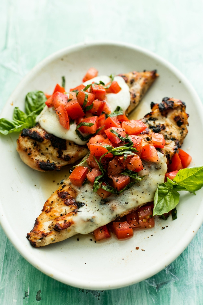 two baked chicken breasts, creamy cheese sauce and tomatoes on top, whats for dinner tonight, garnished with fresh basil leaves