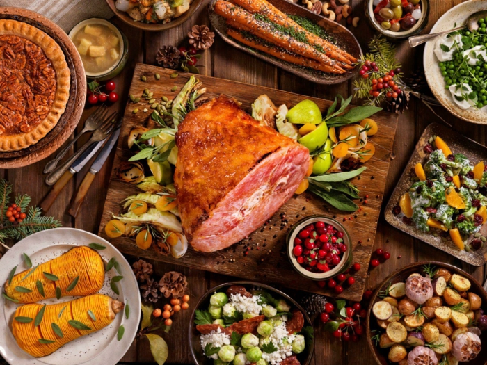 large piece of meat on wooden cutting board, surrounded by different meals, easter dinner recipes, buffet table