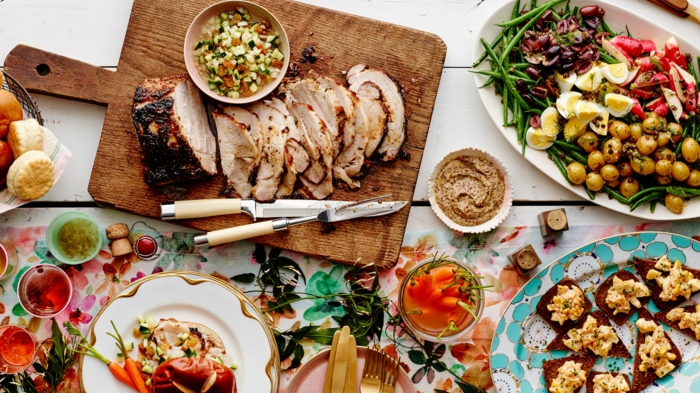 buffet table, sliced ham on a wooden cutting board, easter lunch ideas, surrounded by white plates with different side dishes