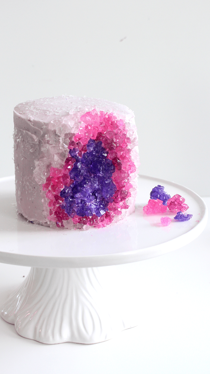 one tier cake, covered with white buttercream, decorated with pink and purple rock candy, geode wedding cake, placed on white cake stand