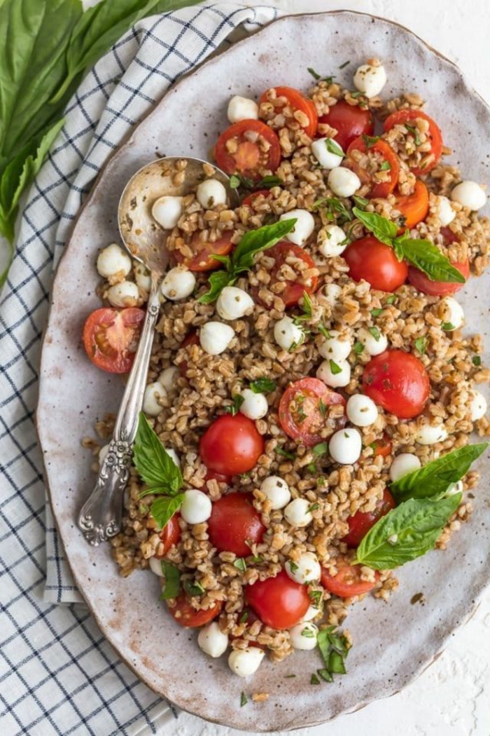 caprese salad with couscous, traditional easter dinner, placed on white plate, halved cherry tomatoes and baby mozzarella
