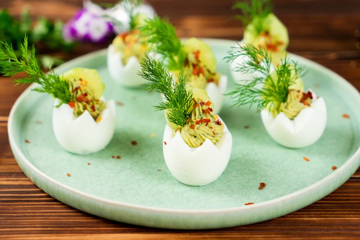 carved out egg whites filled with egg yolk mixture easter eggs arranged on green plate decorated with cucumber dill