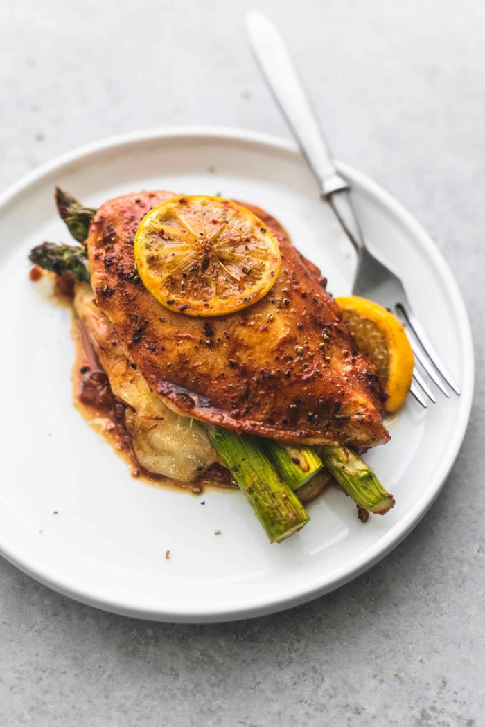 baked chicken breast with lemon slices, placed over asparagus on white plate, what to cook for dinner tonight easy