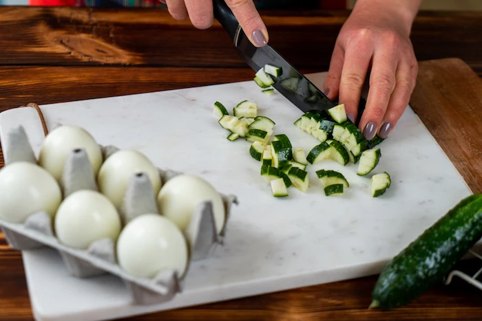 cucumbers being chopped on marble cutting board easter dinner ideas boiled and peeled eggs in a carton on the side