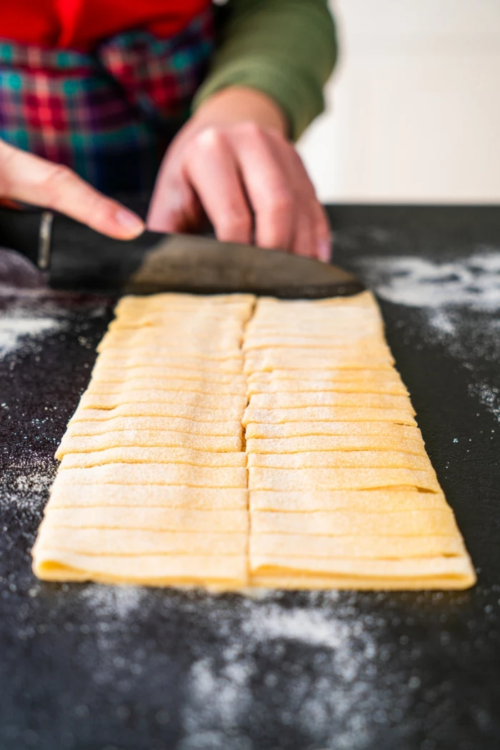dough being cut into thin strips, placed on black surface covered with flour, tagliatele recipe
