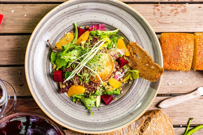 salad with couscous and beets, easter buffet menu, orange slices, bread on the side, placed on grey plate