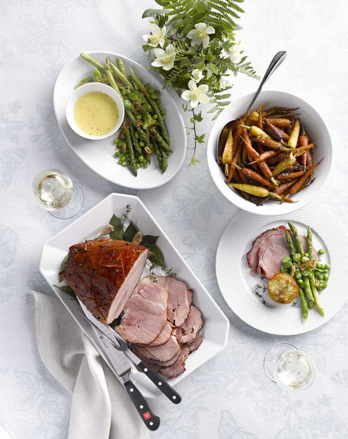 sliced ham placed on white plate, fork and knife on the side, easter buffet menu, roasted pepper and asparagus