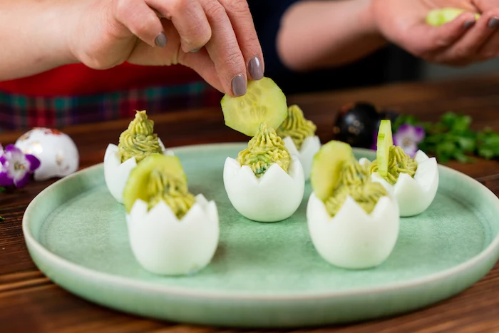 easter eggs being carved out filled with mixture decorated with cucumber slices arranged on mint green plate