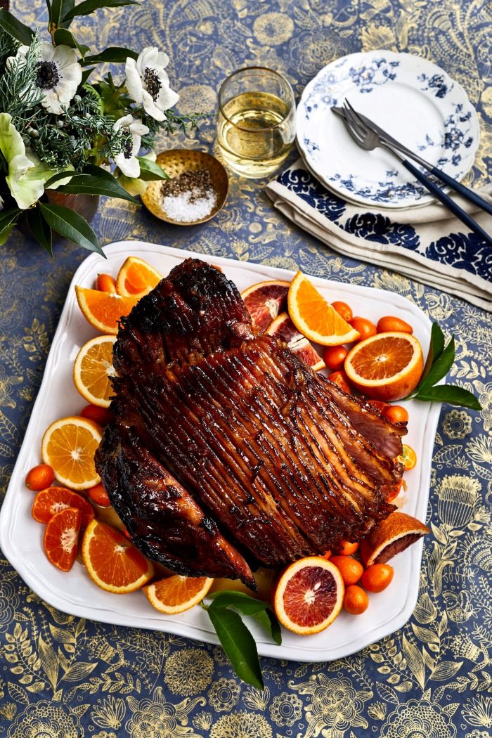 sliced ham placed on a white plate, lemons oranges and cherry tomatoes around it, easter menu ideas 2019