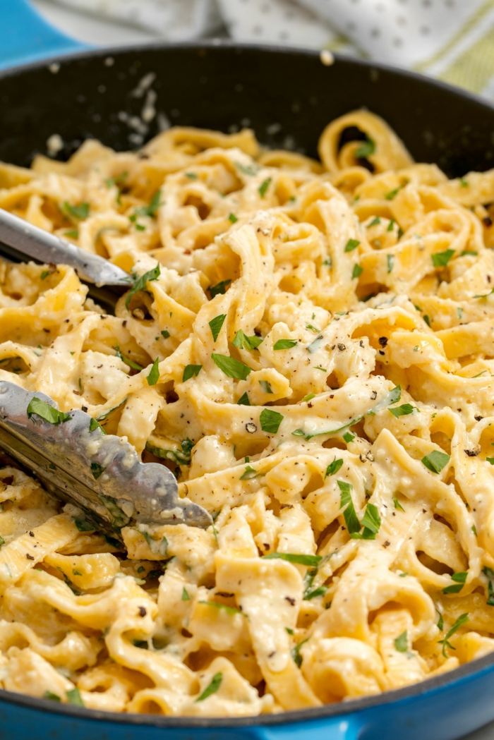 fettucine alfredo, garnished with parsley, cooked in sauce pan and stirred with tongs, good home cooked meals