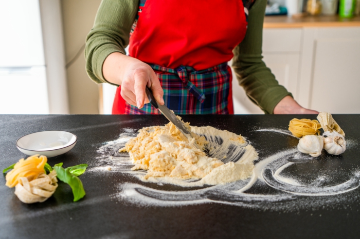 wet and dry ingredients, mixed together on black surface, covered with flour, homemade pasta