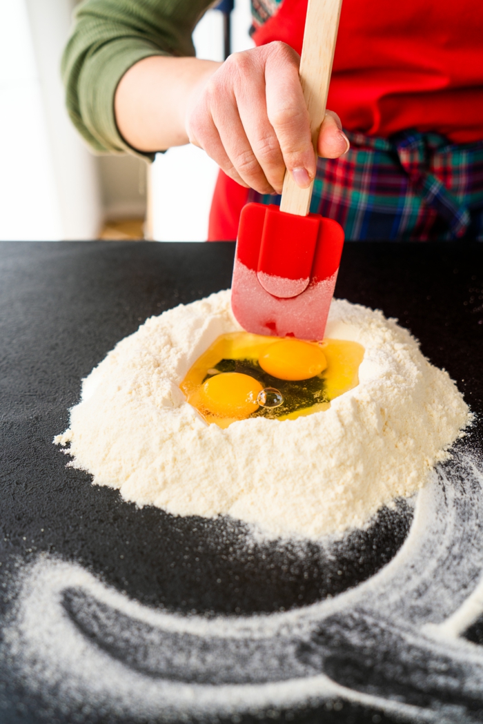 two eggs in the middle of flour, homemade pasta, placed on black surface, formed with red spatula