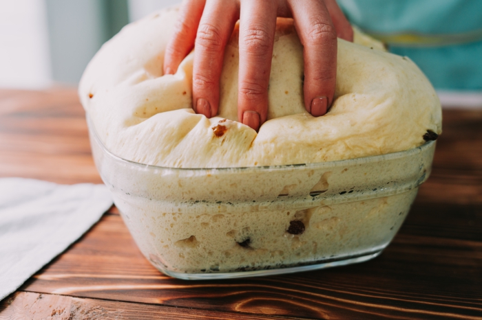 fluffy dough with raisins in glass bowl, placed on wooden countertop, easter bread