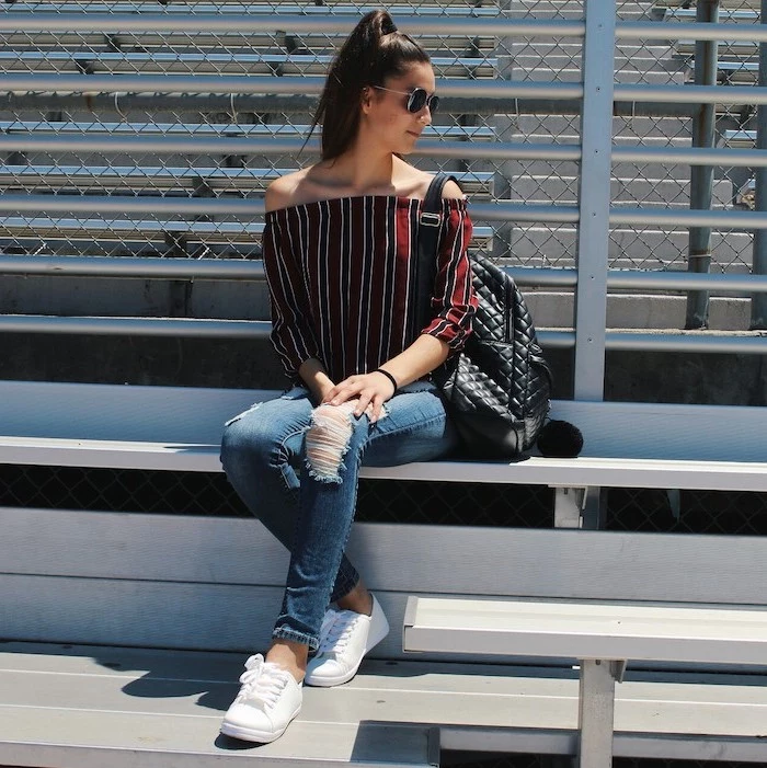 brunette woman sitting on a bench, first day of school outfits, wearing jeans and red and black shirt, white sneakers