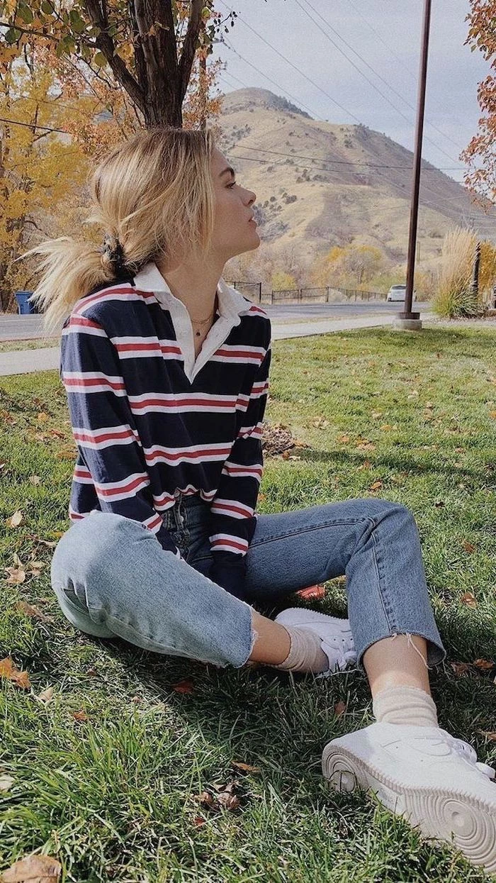 fall outfits for girls, girl sitting on the grass, wearing washed jeans, navy blue and red striped blouse, white sneakers