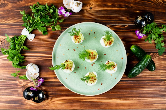 green plate placed on wooden surface easter eggs stuffed with egg yolk mixture decorated with dill cucumber slices